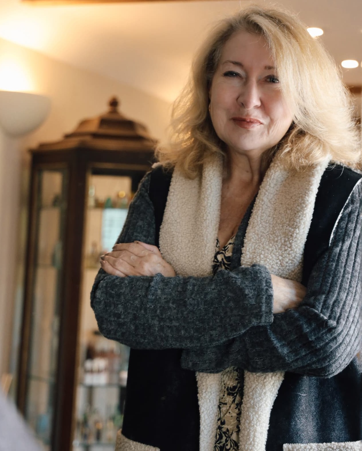 Sharon standing with her arms crossed in a warmly lit room